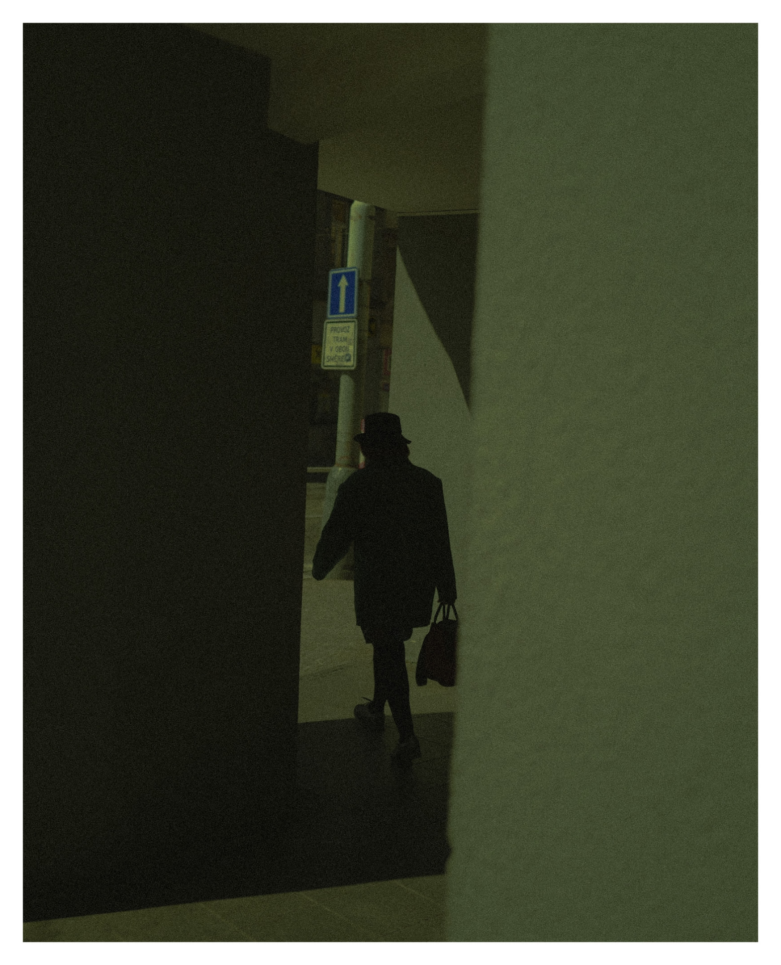 Figure with a hat and bag walking past a narrow gap between walls